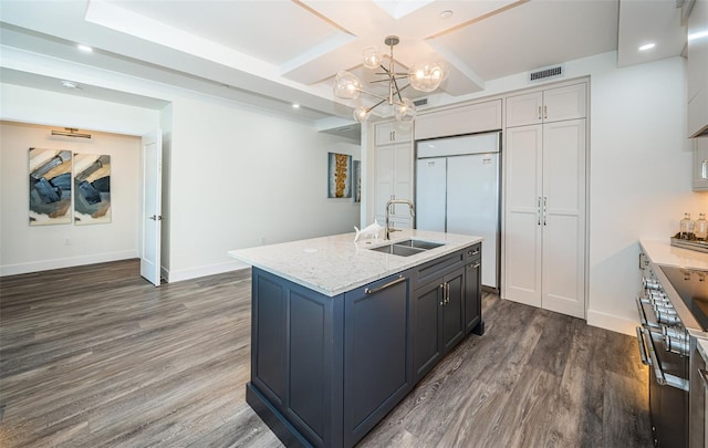 kitchen with light stone countertops, sink, dark hardwood / wood-style floors, decorative light fixtures, and a center island with sink