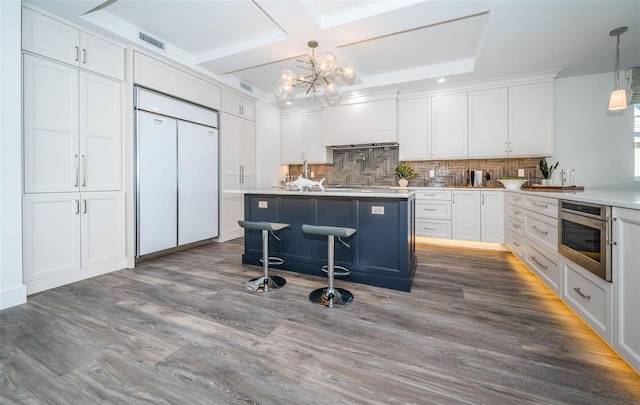 kitchen featuring tasteful backsplash, stainless steel oven, pendant lighting, light hardwood / wood-style flooring, and white cabinetry