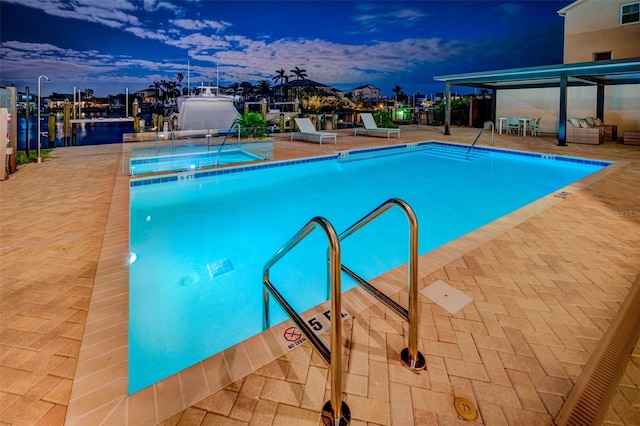 pool at dusk with a water view and a patio