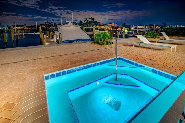 pool at dusk featuring a water view and an in ground hot tub