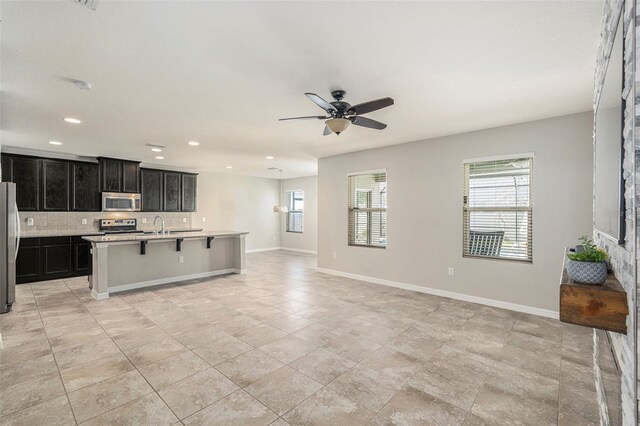 kitchen featuring ceiling fan, backsplash, a breakfast bar, a center island with sink, and appliances with stainless steel finishes