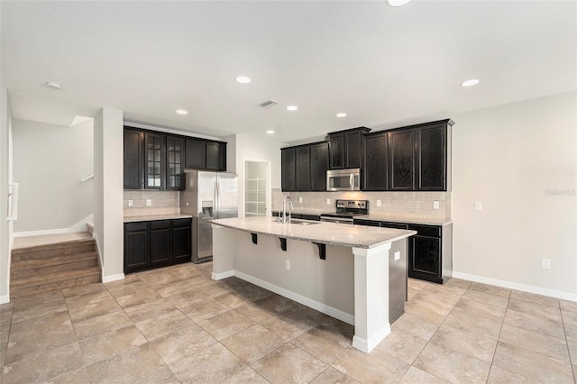 kitchen featuring sink, a kitchen island with sink, stainless steel appliances, a kitchen bar, and decorative backsplash