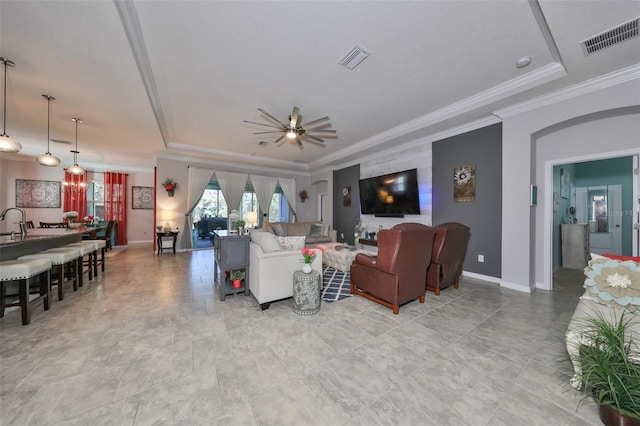 living room with a raised ceiling, ceiling fan, and ornamental molding