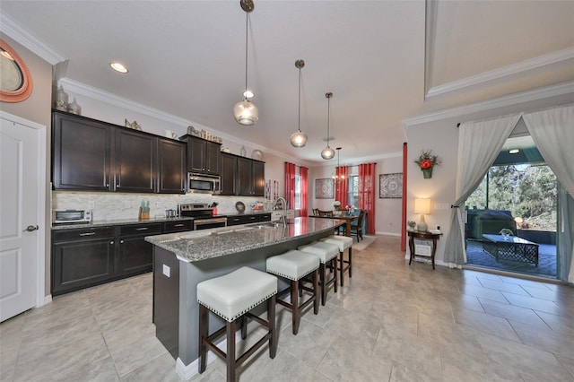 kitchen with stainless steel appliances, stone countertops, decorative light fixtures, a breakfast bar area, and an island with sink