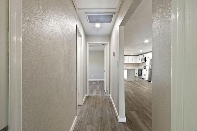 hallway featuring visible vents, baseboards, a textured wall, and wood finished floors