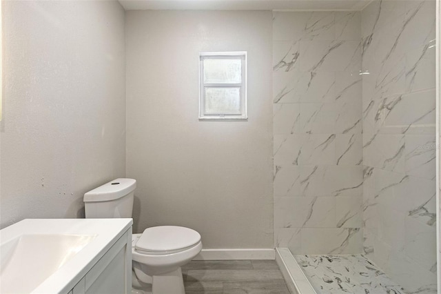 bathroom with vanity, wood finished floors, baseboards, tiled shower, and toilet