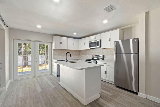 kitchen with appliances with stainless steel finishes, white cabinetry, an island with sink, sink, and backsplash