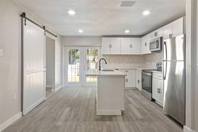 kitchen with sink, white cabinetry, light hardwood / wood-style flooring, an island with sink, and stainless steel appliances