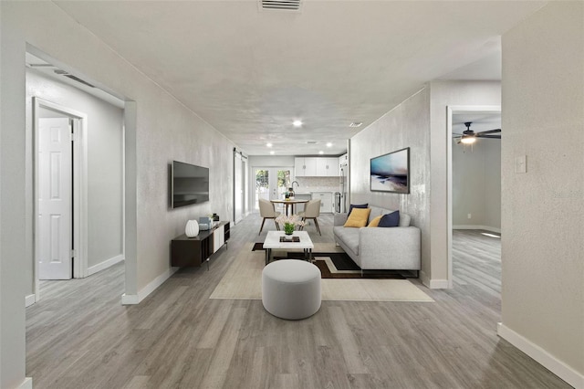 living room with light wood-style flooring, visible vents, and baseboards