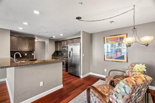 kitchen with appliances with stainless steel finishes, tasteful backsplash, sink, pendant lighting, and dark stone countertops