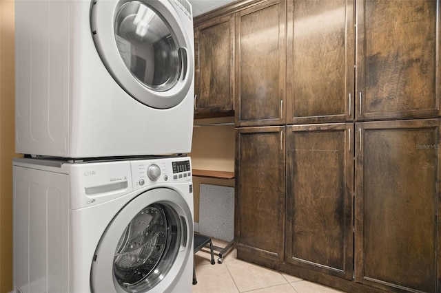 clothes washing area featuring cabinets, light tile patterned flooring, and stacked washing maching and dryer