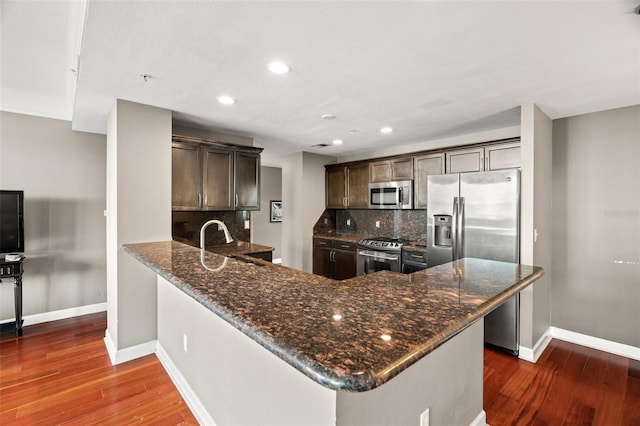 kitchen featuring sink, stainless steel appliances, dark wood-type flooring, tasteful backsplash, and kitchen peninsula