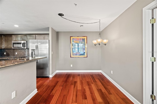 kitchen featuring stainless steel appliances, dark hardwood / wood-style flooring, backsplash, dark stone countertops, and pendant lighting