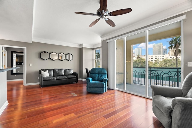 living room with baseboards, ornamental molding, wood finished floors, a view of city, and a ceiling fan