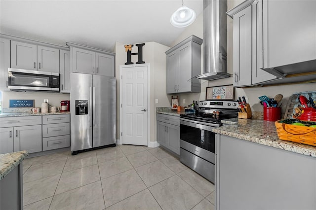 kitchen with wall chimney range hood, gray cabinets, appliances with stainless steel finishes, light tile patterned flooring, and light stone counters