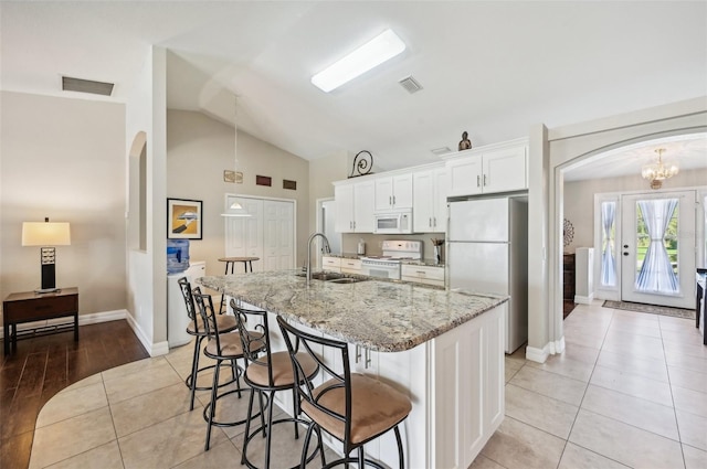 kitchen featuring sink, light stone counters, vaulted ceiling, white appliances, and white cabinets