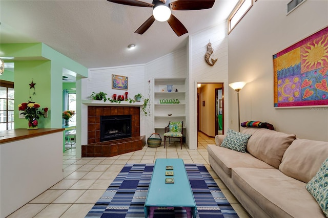 living room with ceiling fan, light tile patterned floors, a textured ceiling, a towering ceiling, and a tiled fireplace