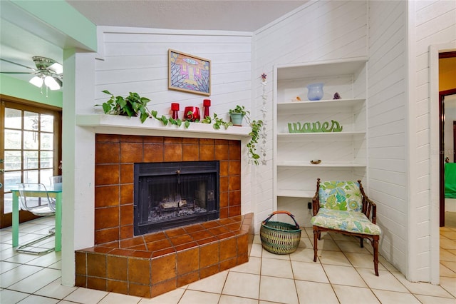 living room with light tile patterned floors, ceiling fan, built in shelves, and a tiled fireplace