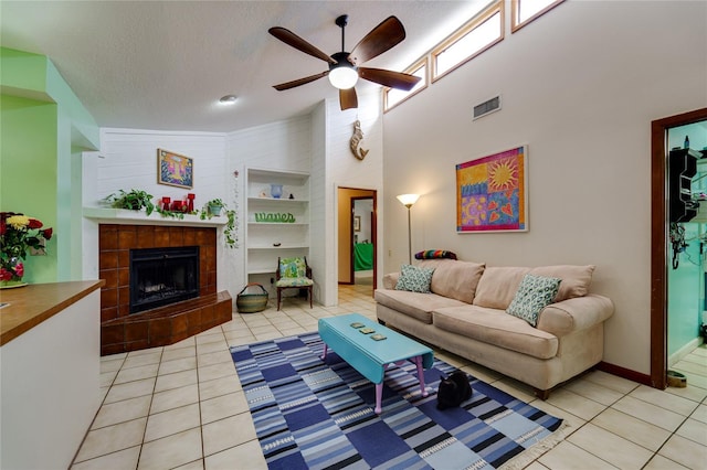 living room with a textured ceiling, light tile patterned flooring, a tiled fireplace, and visible vents