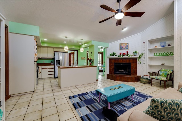 living area with a ceiling fan, a tile fireplace, light tile patterned flooring, and a textured ceiling