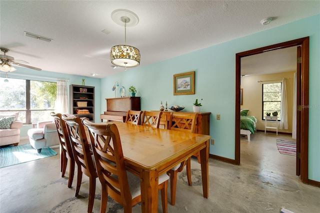 dining room featuring finished concrete flooring, visible vents, ceiling fan, a textured ceiling, and baseboards