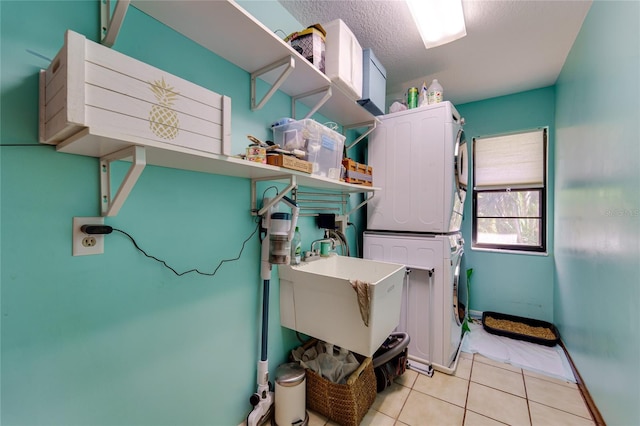 laundry area with stacked washer and dryer, light tile patterned flooring, a sink, a textured ceiling, and laundry area