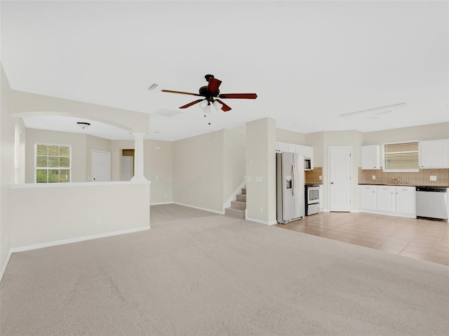 unfurnished living room featuring ceiling fan, light colored carpet, sink, and decorative columns