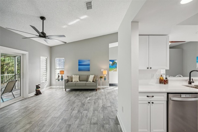 interior space featuring dishwasher, white cabinets, sink, vaulted ceiling, and light wood-type flooring