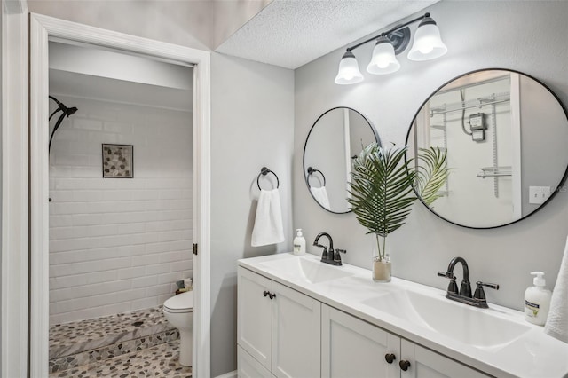 bathroom with a textured ceiling, vanity, a tile shower, and toilet