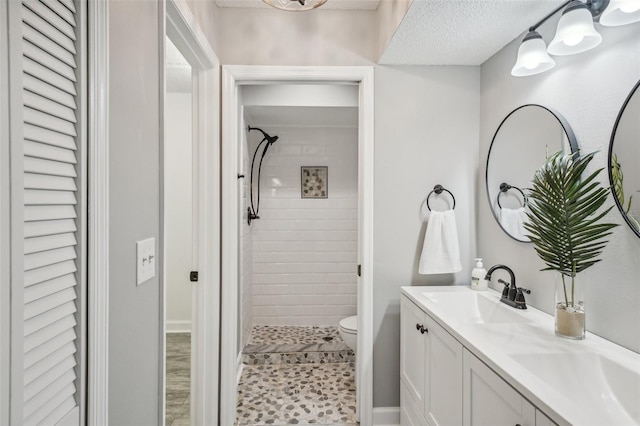 bathroom with a tile shower, vanity, a textured ceiling, hardwood / wood-style floors, and toilet