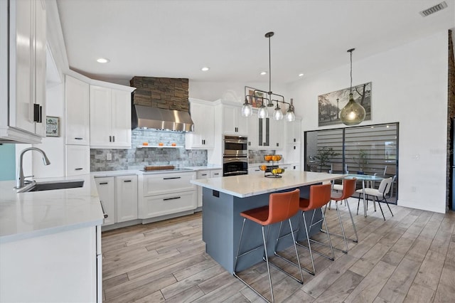 kitchen featuring sink, white cabinetry, vaulted ceiling, a kitchen island, and wall chimney range hood