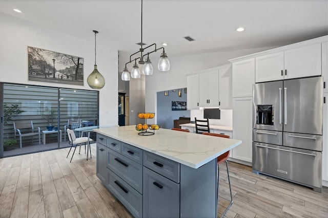 kitchen with a kitchen island, pendant lighting, white cabinetry, high end refrigerator, and light stone counters