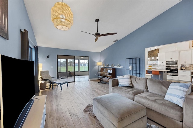 living room featuring ceiling fan, light hardwood / wood-style floors, and vaulted ceiling