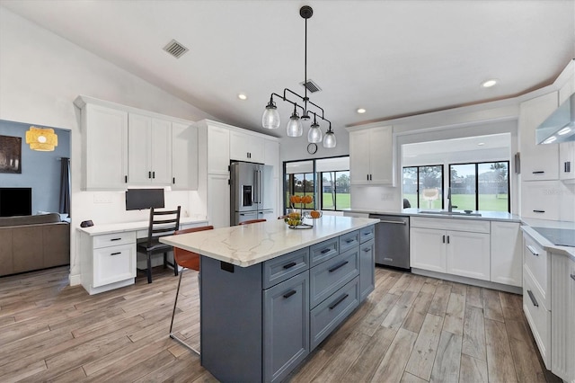 kitchen with a breakfast bar area, appliances with stainless steel finishes, a center island, light stone counters, and white cabinets