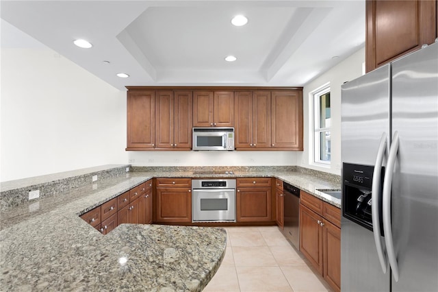 450 Knights Run Ave Unit 407, Tampa, FL 33602 - kitchen with appliances with stainless steel finishes, light stone counters, brown cabinetry, a raised ceiling, and recessed lighting