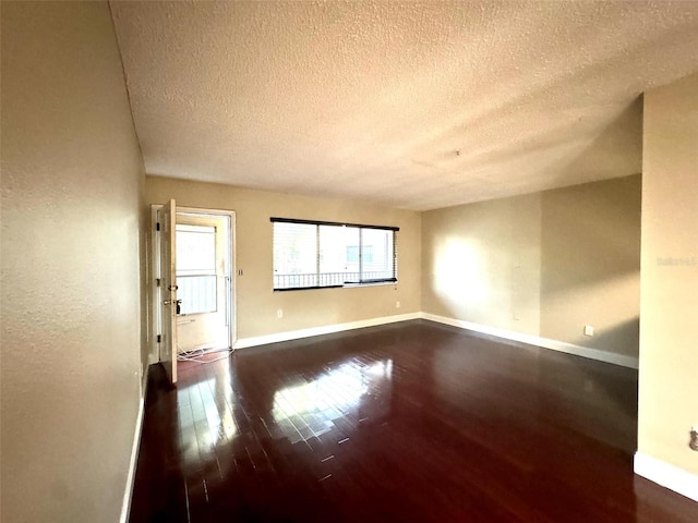 spare room with a textured ceiling, dark wood-style flooring, and baseboards