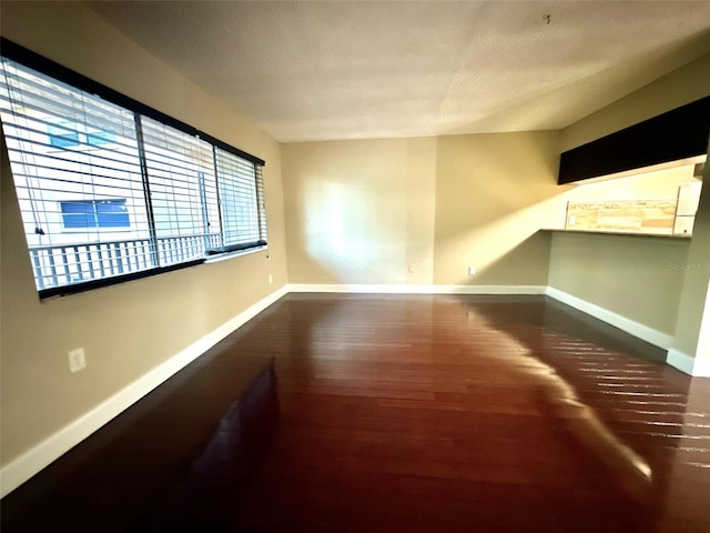 unfurnished room with a textured ceiling, baseboards, and wood finished floors