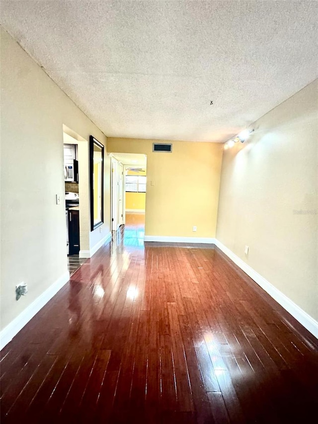 empty room with a textured ceiling, hardwood / wood-style flooring, visible vents, and baseboards