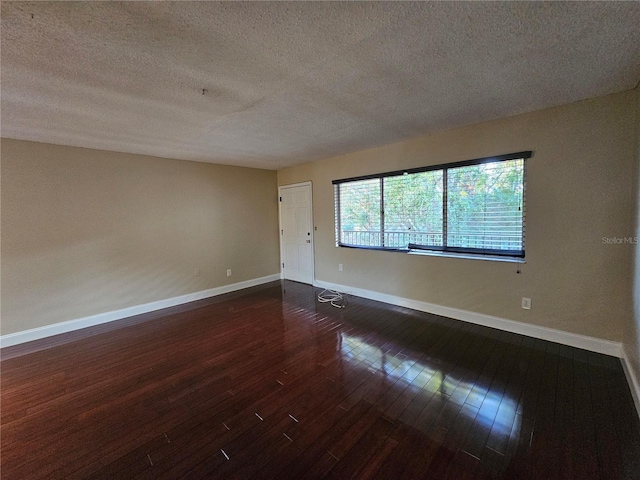 spare room featuring dark wood-style floors, a textured ceiling, and baseboards