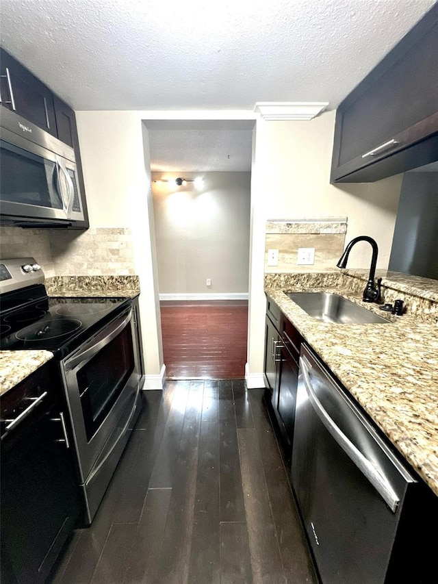 kitchen featuring a textured ceiling, stainless steel appliances, dark wood-style flooring, a sink, and light stone countertops