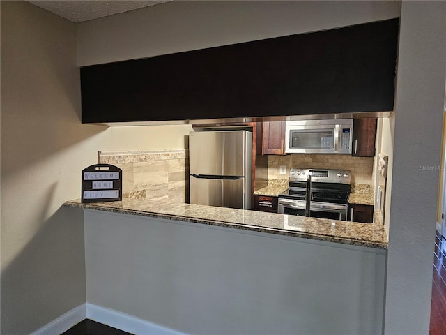 kitchen featuring stainless steel appliances, stone counters, backsplash, and baseboards