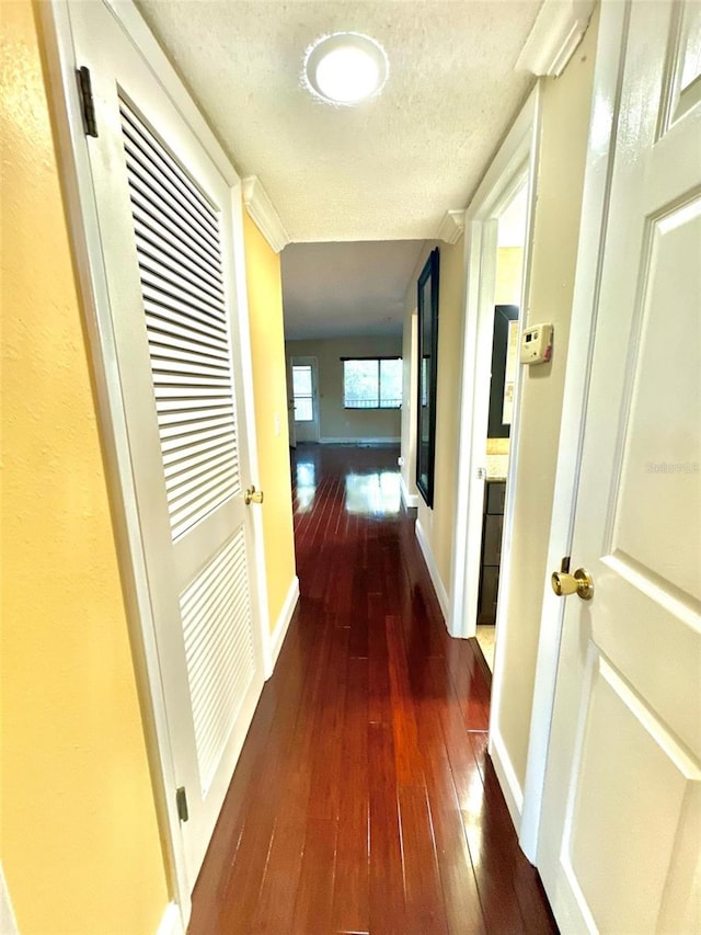 hallway featuring a textured ceiling, baseboards, and hardwood / wood-style flooring