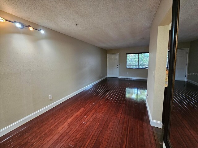 unfurnished room with a textured ceiling, baseboards, and dark wood-type flooring