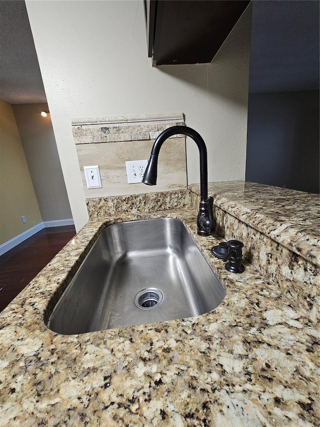 interior details with light stone countertops, a sink, wood finished floors, baseboards, and exhaust hood