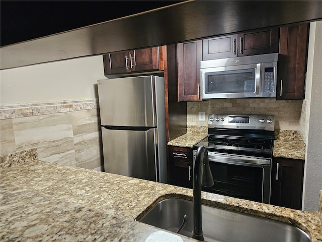 kitchen featuring tasteful backsplash, appliances with stainless steel finishes, a sink, dark brown cabinets, and light stone countertops