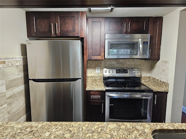 kitchen featuring stainless steel appliances, light stone counters, and dark brown cabinetry