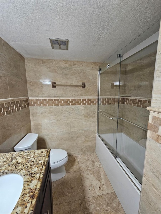 bathroom with toilet, tile walls, visible vents, and a textured ceiling