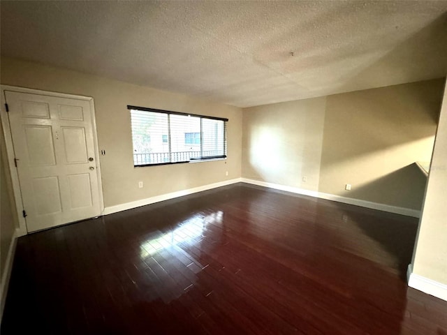 unfurnished room with a textured ceiling, dark wood-type flooring, and baseboards