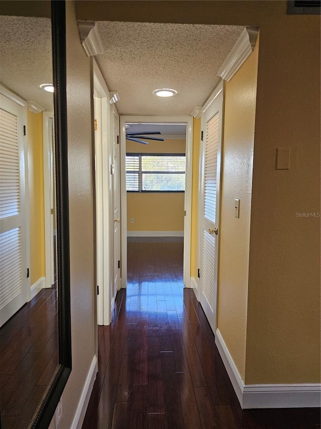 hall featuring dark wood-style flooring, a textured ceiling, and baseboards