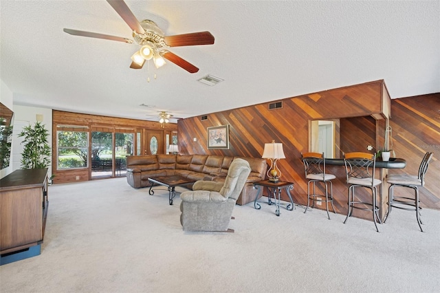 carpeted living room featuring ceiling fan, a textured ceiling, and wooden walls